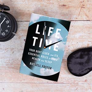 Image of book cover (clock overlayed with clouds reading "Life Time") sitting on a wooden table